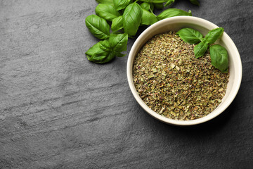 Dry basil in bowl and fresh green leaves on black textured table, flat lay. Space for text