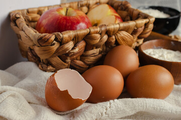 Bakery ingredients for homemade apple desserts with eggs, flour, and fresh fruit, preparing a rustic recipe with natural products on a textured linen cloth