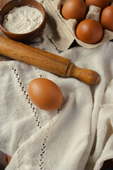 A top-down view of freshly baked ingredients laid out on a linen cloth, a whole brown egg, bowls of flour, and a rolling pin, ready for making homemade pastries and comforting recipes.