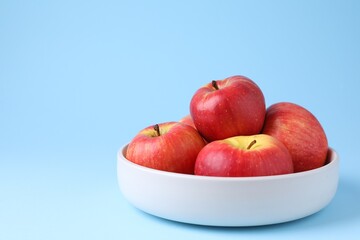 Ripe red apples in bowl on light blue background, closeup. Space for text