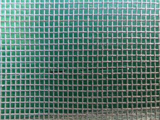 Close-up of mosquito net screen over green wooden Majorcan shutter slats. Protective fine mesh texture, insect protection with ventilation, Mediterranean architecture, grid pattern, outdoor. 