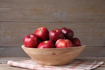 Ripe red apples in bowl on wooden table, closeup