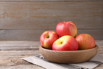 Ripe red apples in bowl on wooden table, closeup. Space for text