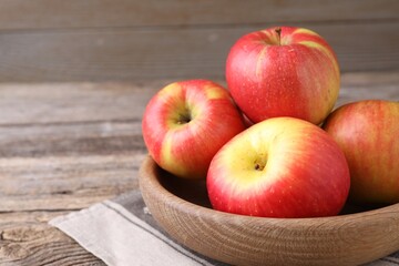 Ripe red apples in bowl on wooden table, closeup. Space for text