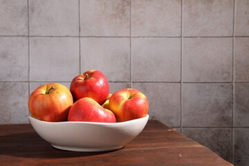 Ripe red apples in bowl on wooden table near grey tiled wall, closeup. Space for text