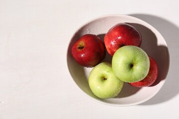 Fresh red and green apples with water drops in bowl on white table, top view. Space for text