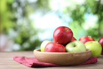 Fresh apples and bowl on wooden table against blurred green background, closeup. Space for text