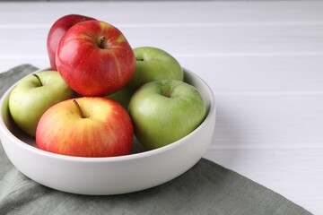 Fresh red and green apples in bowl on white wooden table, closeup. Space for text