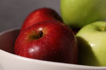 Fresh red and green apples with water drops in bowl against grey background, closeup