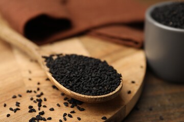Aromatic black caraway in spoon and bowl on wooden table, closeup