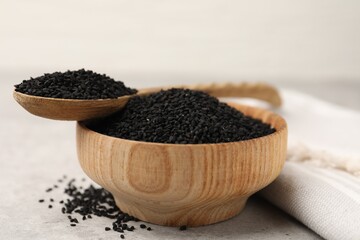 Aromatic black caraway in wooden bowl and spoon on light grey table, closeup