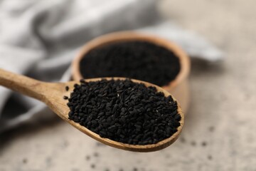 Aromatic black caraway in wooden spoon near bowl at grey table, closeup