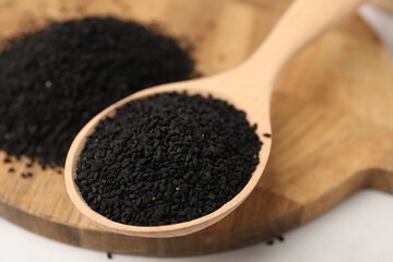 Aromatic black caraway in wooden spoon on white table, closeup