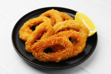 Deep fried squid rings with lemon slice on white tiled table, closeup