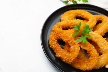Deep fried squid rings with parsley on white tiled table, closeup. Space for text