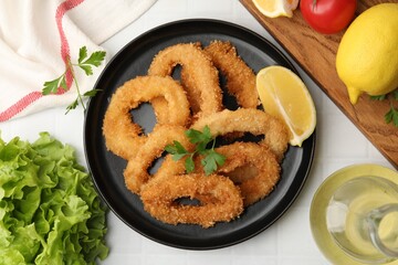 Deep fried squid rings with parsley and lemon slice on white tiled table, flat lay