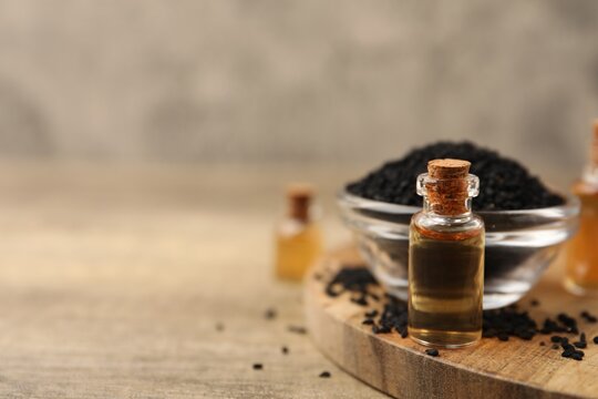 Black cumin seeds and oil on wooden table, closeup. Space for text