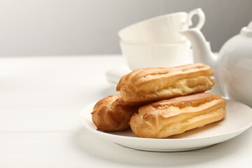 Tasty eclairs served on white wooden table, closeup. Space for text