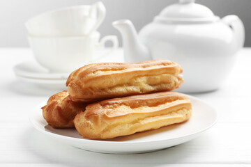Tasty eclairs served on white wooden table, closeup