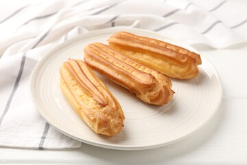 Fresh tasty eclairs on white wooden table, closeup