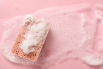 Kitchen sponge with foam on pink background, top view