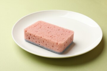 Kitchen sponge and plate on light green background, closeup
