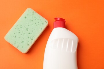 Kitchen sponge and dish soap on orange background, flat lay