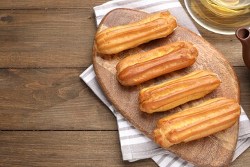 Tasty eclairs and tea on wooden table, flat lay. Space for text