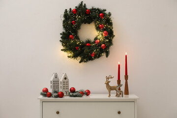 Christmas decor and burning candles on cabinet near white wall indoors