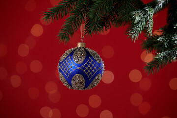 Beautiful ball on Christmas tree branch against red background, closeup. Bokeh effect