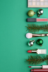 Makeup products and Christmas decor on green background, flat lay. Space for text