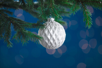 Beautiful ball on Christmas tree branch against blue background, closeup. Bokeh effect