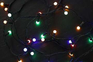 Bright Christmas lights on dark textured table, top view