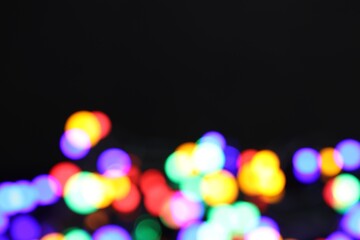 Blurred view of bright Christmas lights on dark background, bokeh effect. Space for text