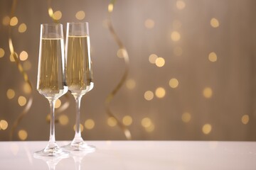 Merry Christmas and Happy New Year. Flute glasses with sparkling wine on white table against blurred lights. Space for text