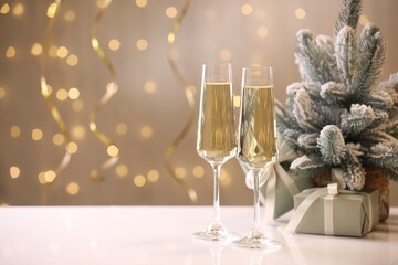 Merry Christmas and Happy New Year. Flute glasses with sparkling wine and festive decor on white table against blurred lights. Space for text