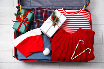 Christmas vacation. Suitcase with Santa hat, clothes, gift boxes and candy canes on floor indoors, top view