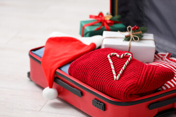 Christmas vacation. Suitcase with Santa hat, clothes, gift boxes and candy canes on floor indoors, closeup
