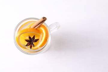Tasty mulled wine with spices and orange slices in glass cup on white table, top view. Space for text