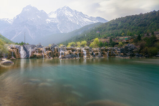 View of cascading waterfalls reflecting the towering snow-capped mountains amidst lush greenery, Lijiang, Yunnan, China.