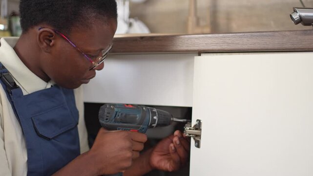 Black female carpenter installing a cabinet door hinge