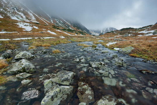 View of a stream flowing through a rocky landscape, with mountains fading into the misty horizon, Rackove pleso tarn, Jamnik, Zilina Region, Slovakia.