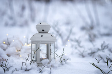 candle lantern stands in the snow in a forest. Christmas background with garland lights and copy space.