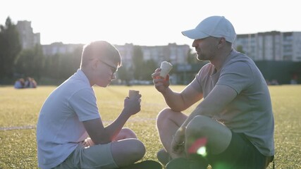 Happy father and son spending quality time outdoors, joking and eating ice cream during Father’s Day.