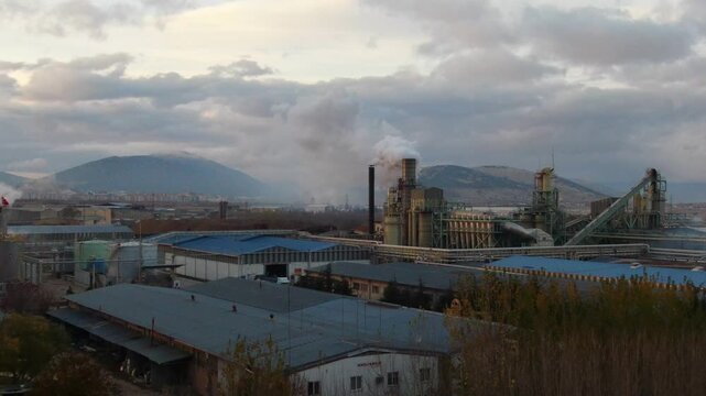Smoke rises from the chimney of the industrial plant, polluting the environment and the mountains. The concepts of industrialization and air pollution.