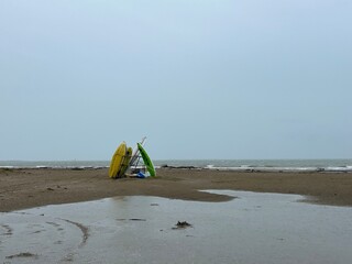 Colorful kayaks stacked on a deserted beach with puddles and cloudy weather by the sea