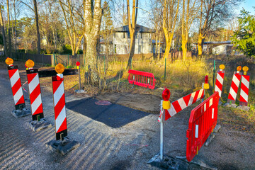 Road repair site with warning barriers and lights marking freshly patched asphalt area on street