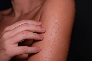 Young woman touching wet skin on her shoulder after shower on a dark background. Close-up of hydrated skin with water droplets, showing natural beauty and body care 