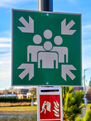 Emergency assembly point sign with directional arrows and fire safety symbol outdoors