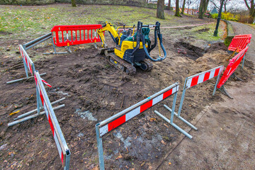 Mini excavator at fenced-off construction site in park during ground excavation work